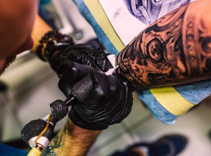 Professional tattooist creating a black and white detailed skull tattoo
