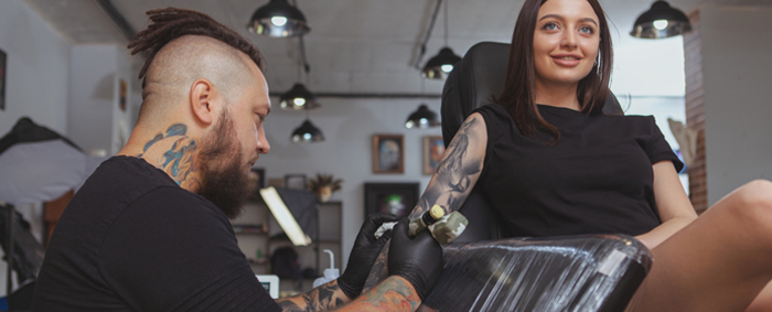 Männlicher Tätowierer tätowiert weiblichen Kunden während einer Eröffnungsparty im Tattoostudio