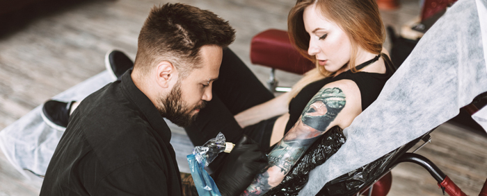 Male artist working on a females arm sleeve tattoo
