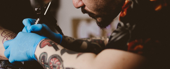 A male tattooist with a moustache tattooing
