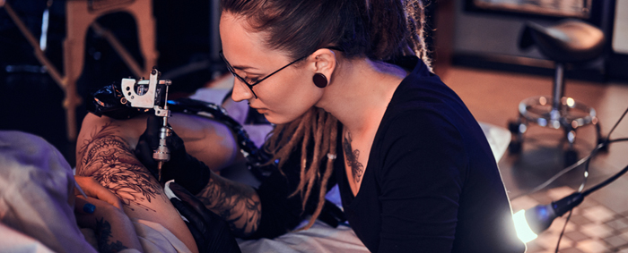 A female tattoo artist tattooing a client