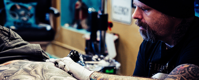 Male tattoo artist with hat working on body tattoo