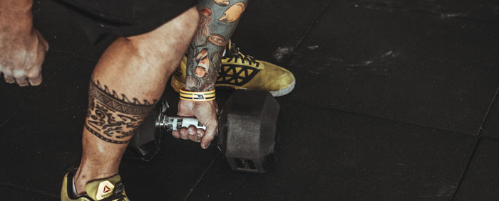 Tattooed man about to lift a dumbbell from the floor.