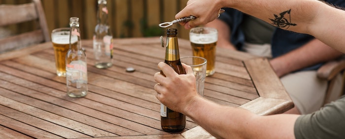 Eine Flasche Bier wird von einem tätowiertem Mann geöffnet.