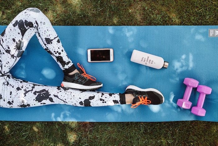 Resting legs on a yoga matress next to dumbbells, bottle of water and mobile phone.