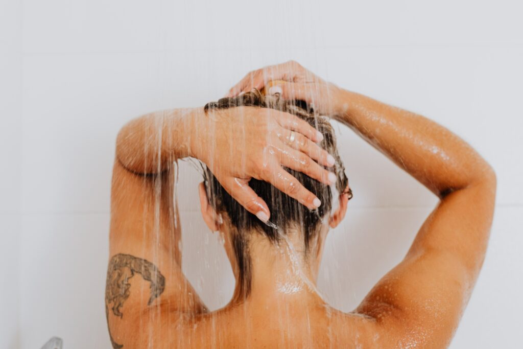 A tattooed person from the back showering.